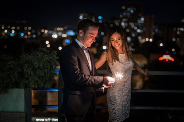 Romantic newlyde couple standing on the roof top in the city in the night celebrating their love with sparklers